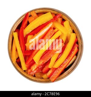 A heap of sliced bell peppers in a wooden bowl. Sweet pepper or capsicum cut in colorful stripes. Fresh yellow, orange and red fruits. Stock Photo