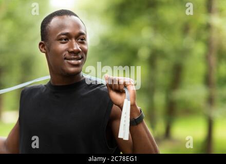 Smiling sporty guy with jumping rope training at park Stock Photo