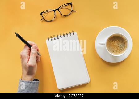 Man's hand hoding pen near blank notepad on the table with coffee and glasses, top view Stock Photo