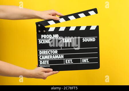 Female hands holding clapper board on yellow background Stock Photo