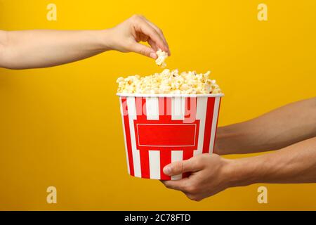Male and female hands and bucket with popcorn on yellow background Stock Photo
