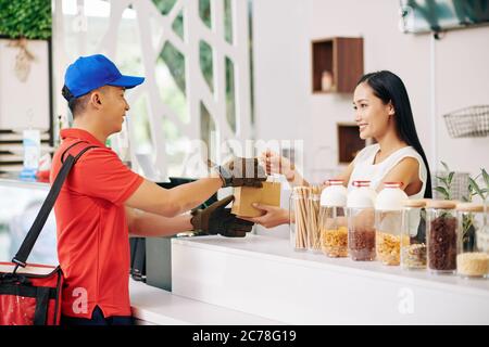 Smiling pretty small coffeeshop owner giving packed order to delivery man Stock Photo