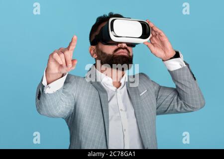 Businessman wearing virtual reality headset and pointing at imaginary screen over blue background Stock Photo