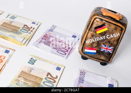 Bamberg, Deutschland. 13th July, 2020. Bamberg, Germany July 13, 2020: Symbolic images - 2020 Several thousand euros in cash with the values of 500 euros, 200 euros, 100 euros and 50 euros lie on a white background, next to it a miniature suitcase with the national flags of, Germany, England and Netherlands, | usage worldwide Credit: dpa/Alamy Live News Stock Photo