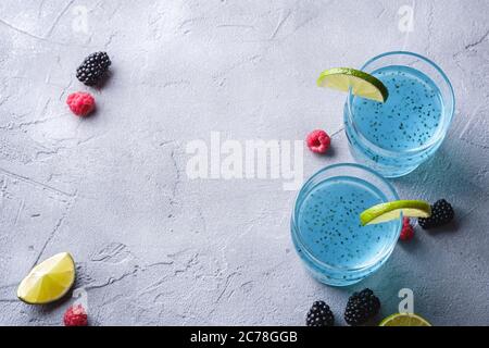 Tasty blue colored cocktail drink with basil chia seeds, citrus lime slice, raspberry and blackberry berries in two glass, healthy summer beverage