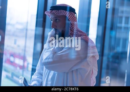 Middle Eastern businessman talking on the phone and looking out the window in his office. Businessman Arabic using mobile phone for connection to comm Stock Photo