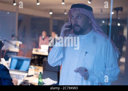 Middle Eastern businessman talking on the phone and looking out the window in his office. Businessman Arabic using mobile phone for connection to comm Stock Photo