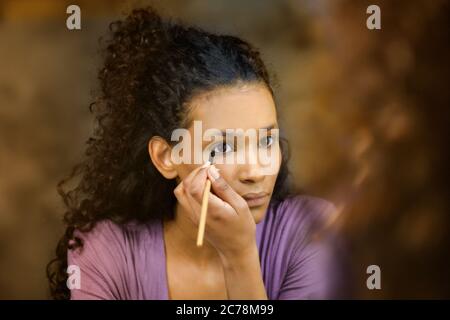 Attractive young black woman doing her makeup carefully applying eyeliner with a pencil to her lower lid in a beauty concept Stock Photo