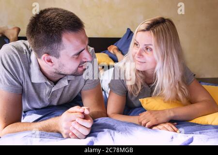Millenial couple of man and woman lying on the bed at home and looking to each other. Stock Photo