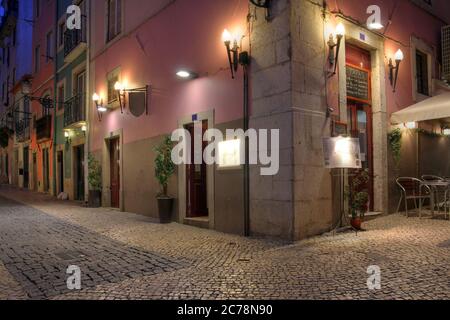 Night scene in Chiado neighbourhood, Lisbon, Portugal, featuring a corner tapas restaurant. The narrow cobbled streets, and tall stone buildings with Stock Photo