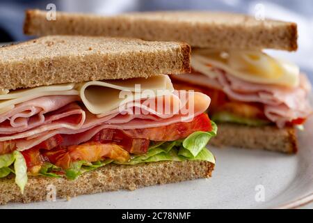 Sandwich with ham, cheese, lettuce and tomato on whole grain bread cut in half on a plate Stock Photo