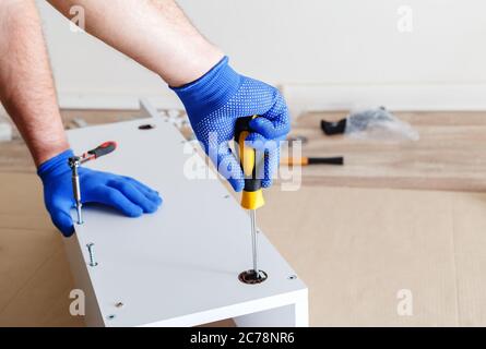 Furniture assembly. Male hands in blue gloves master collects furniture using screwdriver tools, instrument at home. Moving, home improvement Stock Photo