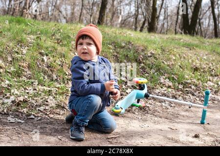 A little boy in an orange hat fell from a scooter. Children's trauma. Falling a child from a scooter. Stock Photo