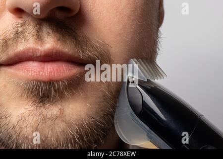 A man shaves his beard with a trimmer razor. Modeling beard, masculine style, facial hair care, morning routines in the bathroom Stock Photo