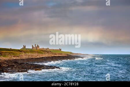 Looking north from Craster along St Oswald's Way footpath and rocky shoreline towards Dunstanburgh Castle, England Stock Photo