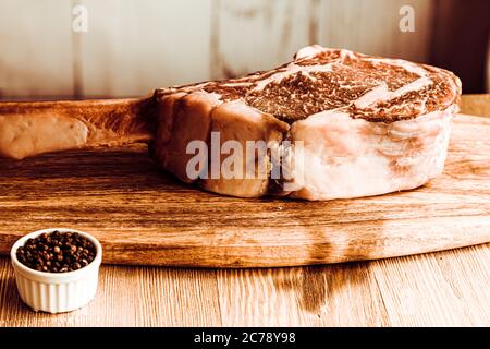Dry aged raw tomahawk beef steak on wooden board and pepper Stock Photo