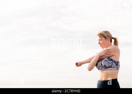 beautiful blonde sportswoman stretching with the sky in the background at dawn, healthy lifestyle and sports concept, copy space for text Stock Photo