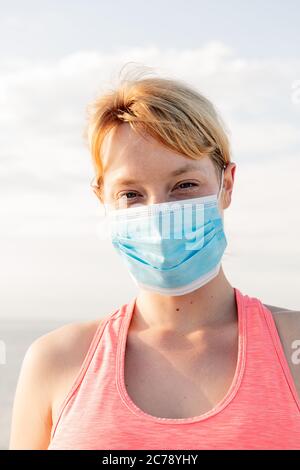 vertical portrait of a beautiful blonde woman with a protective mask with the sky in the background, concept of prevention and health care Stock Photo