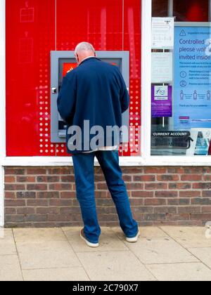 A casually dressed senior man using a Santander ATM cash machine Stock Photo