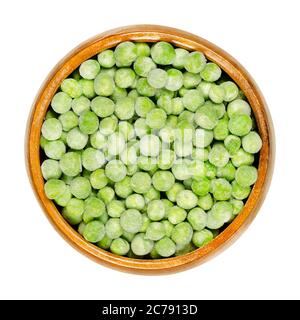 Frozen green peas in wooden bowl. Small spherical seeds of the pod fruit Pisum sativum, frozen to keep the legumes fresh. Closeup, from above. Stock Photo