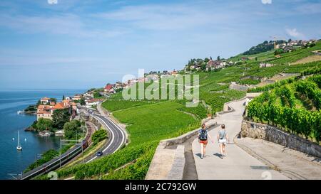 Lavaux Switzerland , 26 June 2020 : Two tourists hiking on a beautiful path in middle of Lavaux terraced vineyards and Rivaz village on Lake Geneva si Stock Photo