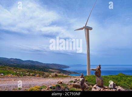 Single windmill turbine, road and balancing stones on hilltop of seashore in colorful landscape at dynamic blue sky on clear sunny summer day. Stock Photo