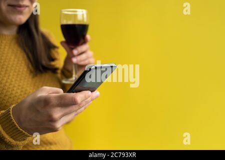 Woman in yellow sweater using phone and holding glass of red wine Stock Photo