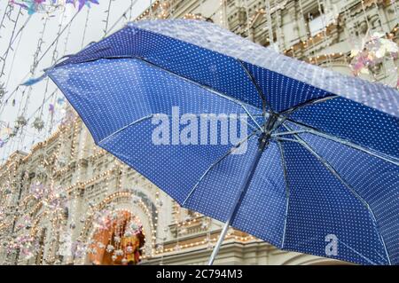Close-up of an open blue umbrella with small polka dots, in the rain in the open air against the background of a city street. Stock Photo