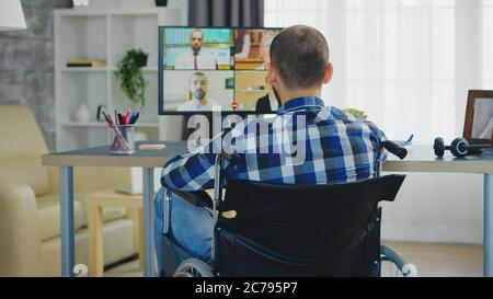 Freelancer in wheelchair waving during a business video call while working from home office. Stock Photo