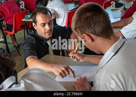 Male teacher coaching one to one a teenage boy student 15-17 years with his study work in secondary high school classroom Stock Photo