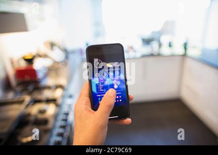 POV Man adjusting climate control from smart phone in kitchen Stock Photo