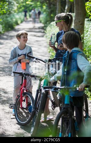 Mother and sons drinking water on bike ride in sunny park Stock Photo