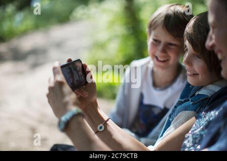 Mother and sons video chatting with friends on smart phone in park Stock Photo
