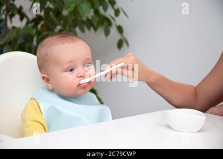 First feeding of baby boy, eat yoghurt, dirty mouth, holds spoon Stock Photo