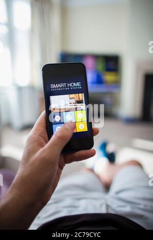POV Man using home automation on smart phone in living room Stock Photo