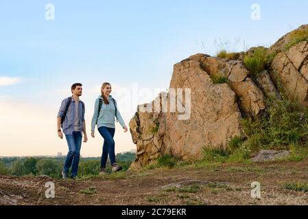 Young Happy Travelers Hiking with Backpacks on the Rocky Trail at Summer Sunset. Family Travel and Adventure Concept. Stock Photo