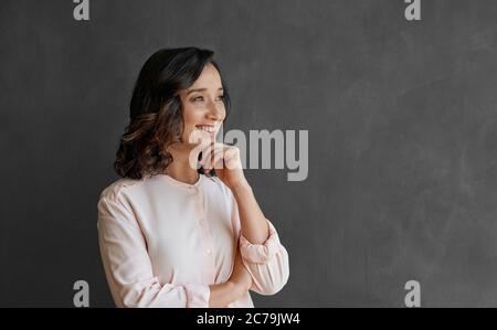 Smiling young Asian businesswoman dreaming up new ideas for her business while standing in front of a blank office chalkboard Stock Photo