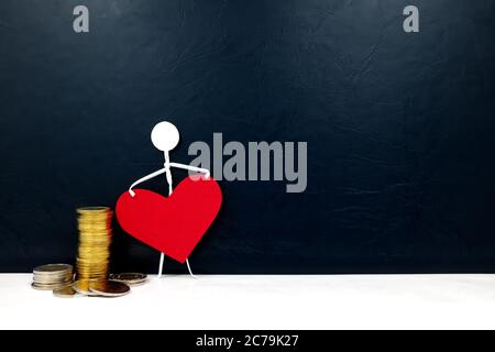 Human stick figure holding a red heart shape with gold coins on side. Cost of healthcare service and healthy wealthy concept. Stock Photo