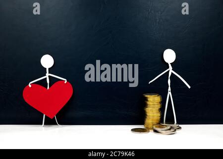 Human stick figure holding a red heart shape and another with gold coins. Money versus love, family or career, and health over economy concept. Stock Photo