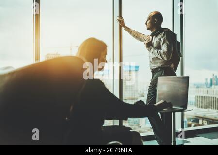 Two silhouettes near the panoramic window of a business office skyscraper: a man entrepreneur aloof, leaning against the window bar Stock Photo