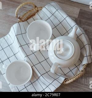 Flat lay of white tea pot and cups on rattan tray on wood Stock Photo