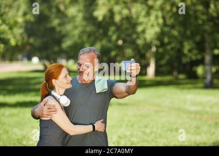 Loving mature couple looking at each other and embracing while posing for selfie in park after sports training Stock Photo