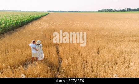 Happy young family walks in yellow wheat field near corn with baby. Copy space. Stock Photo