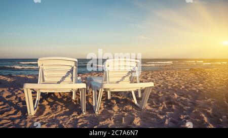 Two deckchairs on the sandy beaches for tourists to sit and relax with soft ocean waves breaking on beach Stock Photo