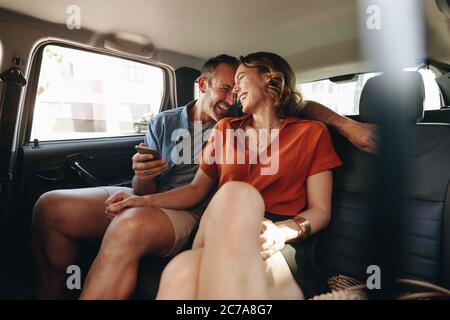 Couple in rear seat of car talking and smiling. Man and woman on commuting in the city by a taxi. Stock Photo