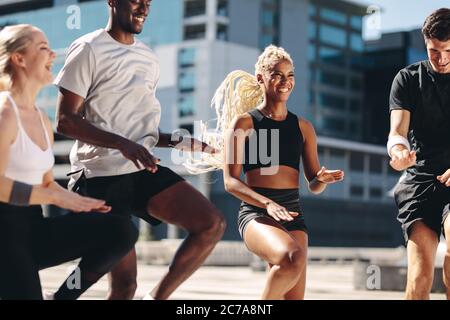 Group of men and women doing exercising together in the city. Multi-ethnic friends workout together and smiling. Running on the same place workout. Stock Photo