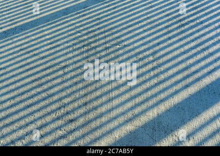 Gap step diagonal shadows from sunlight on a scratched concrete surface on a sunny day. Ascending line shadows of fence poles. Geometric background. Stock Photo