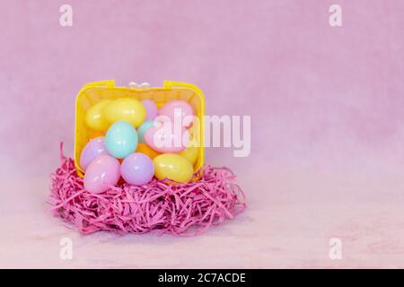 Festive Easter decorations and pink background. Yellow basket filled with plastic easter eggs on pink paper grass. Stock Photo