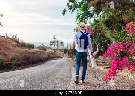 Man traveler walks along road in Akrotiri village on Santorini island Greece. Tourist backpacker admires flowers Stock Photo