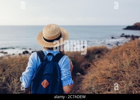 Woman traveler with backpack walking on beach by sea coastline. Tourism, traveling. Summer vacation